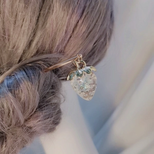 Detail einer goldenen Haarnadel mit einem durchsichtigen weißen Erdbeeranhänger am Zopf