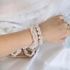 Detailed view of layered cream white pearl bracelets on wrist with elegant lace background