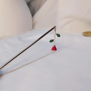 Detailed close-up of a golden hair pin featuring a red rose and green enamel leaves