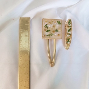 Detail view of handmade resin hair clips with green dried flowers and gold leaf on white fabric