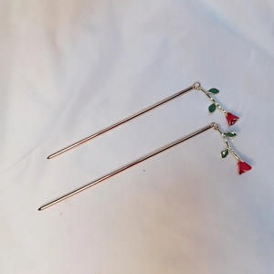 Elegant gold metal hair stick with red rose bud and green leaves on white background