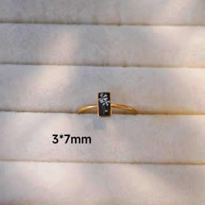 Nahaufnahme eines goldenen Rings mit rechteckigem schwarzem Inlay und weißen Blumen