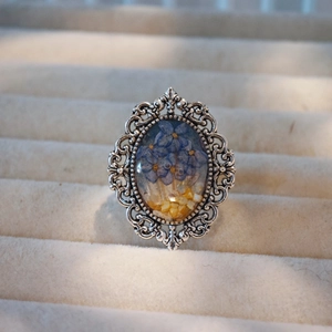 Macro shot of oval resin ring featuring blue dried flowers and vintage silver filigree