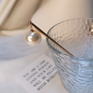 Détail d'un pic à cheveux élégant en or rose avec perle sur le rebord d'un verre