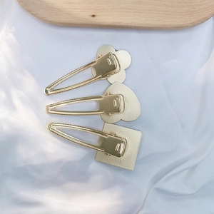 Close-up of three pale gold metal BB hair clips with floral, heart and square base plates
