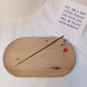 Minimalist golden hair stick with a red rose pendant on a decorative wooden tray