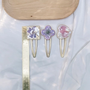 Close-up of resin hair clips with dried flowers and pearls next to a measurement ruler