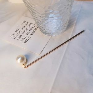 Pic à cheveux doré minimaliste avec élégante perle blanche sur un fond de tissu blanc