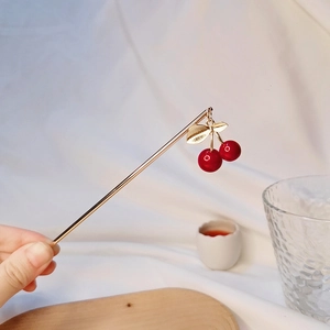 Détail d'un pic à cheveux en métal doré avec pendentifs cerises rouges et feuilles ciselées