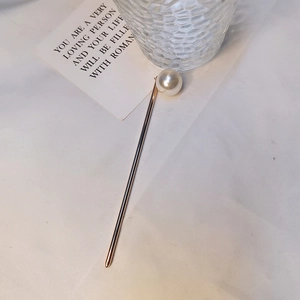 Vue détaillée de l'épingle à cheveux dorée ornée d'une grande perle blanche sur tissu doux