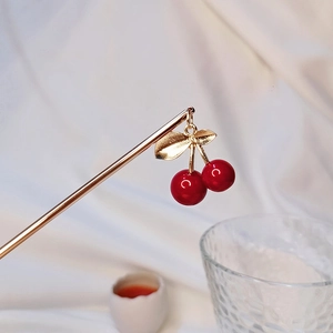 Vue détaillée d'un pic à cheveux cerise dorée fait main avec pendentifs rouges sur soie