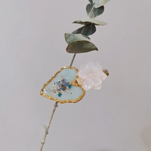 Detail of handmade resin heart hair clip with blue dried flowers and gold foil on leaves