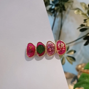 Détail de barrettes en résine avec fleurs séchées et pierres roses montées sur métal doré