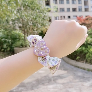 Detail showing a purple floral scrunchie with a dried flower heart charm on wrist