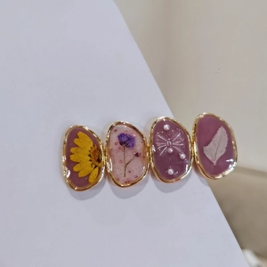 Handmade resin hair clip with dried flowers and golden frame on a clean white surface