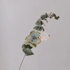 Detail of handmade resin hair clip with blue dried flowers in a golden heart frame