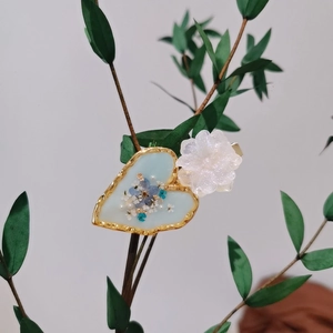 Handmade heart-shaped floral hair clip with blue dried flowers on a green branch