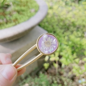 Detailed close-up of a purple resin hair clip with dried daisies and pearls in nature