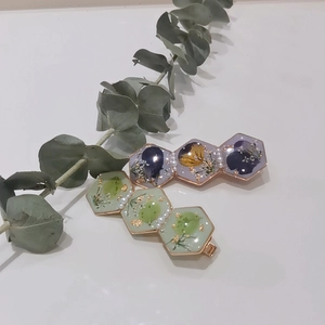 Close-up of resin hair clips with dried flowers, gold foil, and pearls on white background