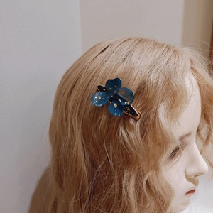 Detail of blue flower resin hair clip with gold foil on blonde mannequin hair