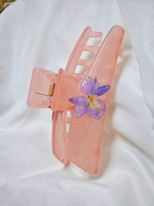 Detail of a resin hair claw clip with preserved purple flowers on soft white fabric