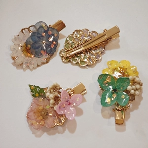 Close-up of four handmade resin hair clips with dried flowers and gold foil accents