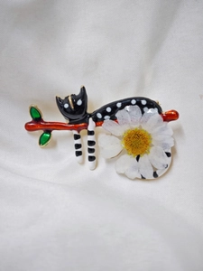 Détail macro d'une broche chat en émail avec marguerite sur une branche marron