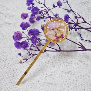 Détail d'une barrette dorée avec fleurs séchées incrustées dans la résine ronde