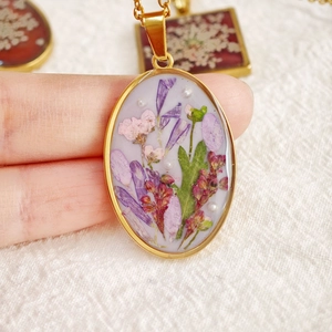 Macro shot of handmade dried flower necklace with purple petals in golden oval frame