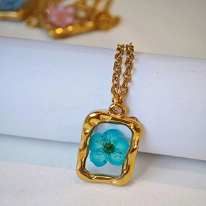 Dettaglio del ciondolo rettangolare vintage dorato martellato con un vero fiore blu