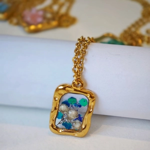 Dettaglio del ciondolo rettangolare dorato in resina con fiori secchi e glitter blu