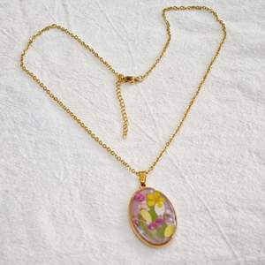 Macro shot of oval resin pendant featuring delicate dried flowers on a gold chain
