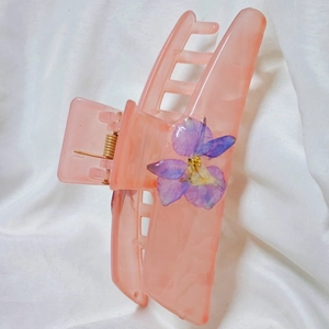 Pink translucent resin hair claw clip with purple dried flowers on white fabric