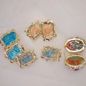 Dettaglio di orecchini artigianali in resina con fiori secchi veri e bordo dorato