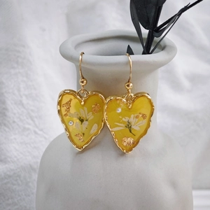Détail de boucles d'oreilles cœur faites main avec résine jaune, fleurs et perles