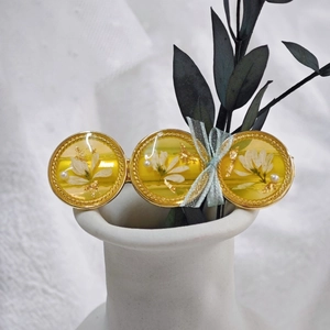 Détail de la barrette en résine avec fleurs séchées, feuilles d'or et nœud papillon