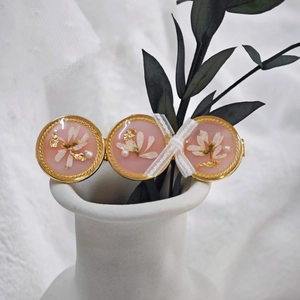 Détail de la barrette en résine rose avec fleurs séchées, feuilles d'or et perles