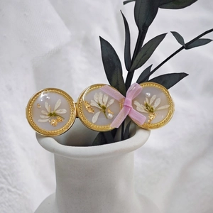 Détail d'une barrette faite main avec fleurs séchées, bordure dorée et nœud en ruban rose