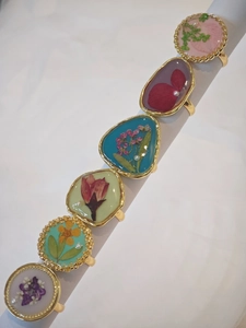 Detailed close-up of six handmade resin rings with pressed dried flowers and small pearls