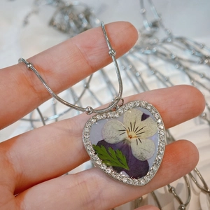 Close-up of heart-shaped pendant with dried pansy flower and sparkling crystal frame