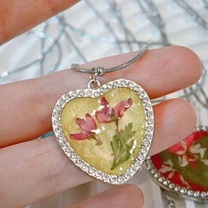 Macro detail of heart resin pendant with pink dried flowers and rhinestone trim