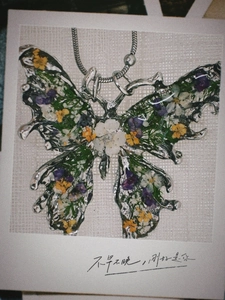 Detail of butterfly pendant with colorful dried flowers embedded in clear resin and silver chain