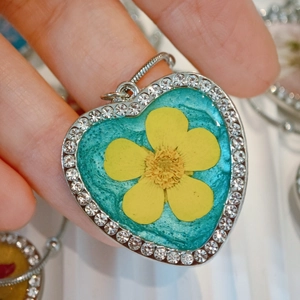 Detailed close-up of heart-shaped resin pendant with yellow flower and rhinestones