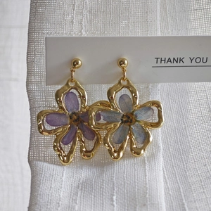 Macro shot of handmade gold earrings with real dried flowers in purple and blue resin