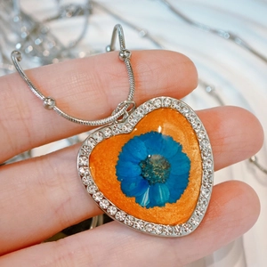 Detail of heart-shaped necklace with blue dried flower and rhinestones on snake chain