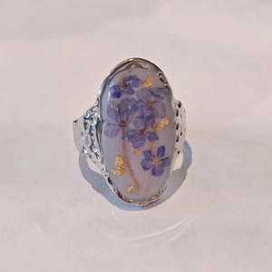 Detail of oval silver ring featuring purple dried flowers and gold leaf inside the resin