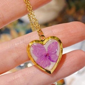 Macro detail of handmade heart necklace with purple dried flower and golden frame