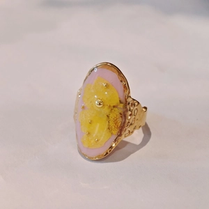 Close-up of handmade gold ring with pink resin, yellow dried flowers and hammered texture