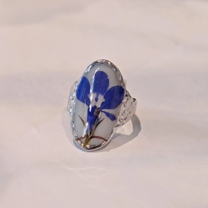 Close-up of handmade oval ring with blue dried flowers and silver hammered texture