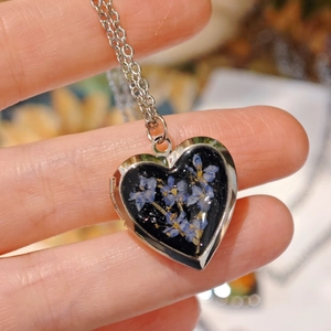 Macro shot of heart-shaped locket with blue dried flowers in polished stainless steel